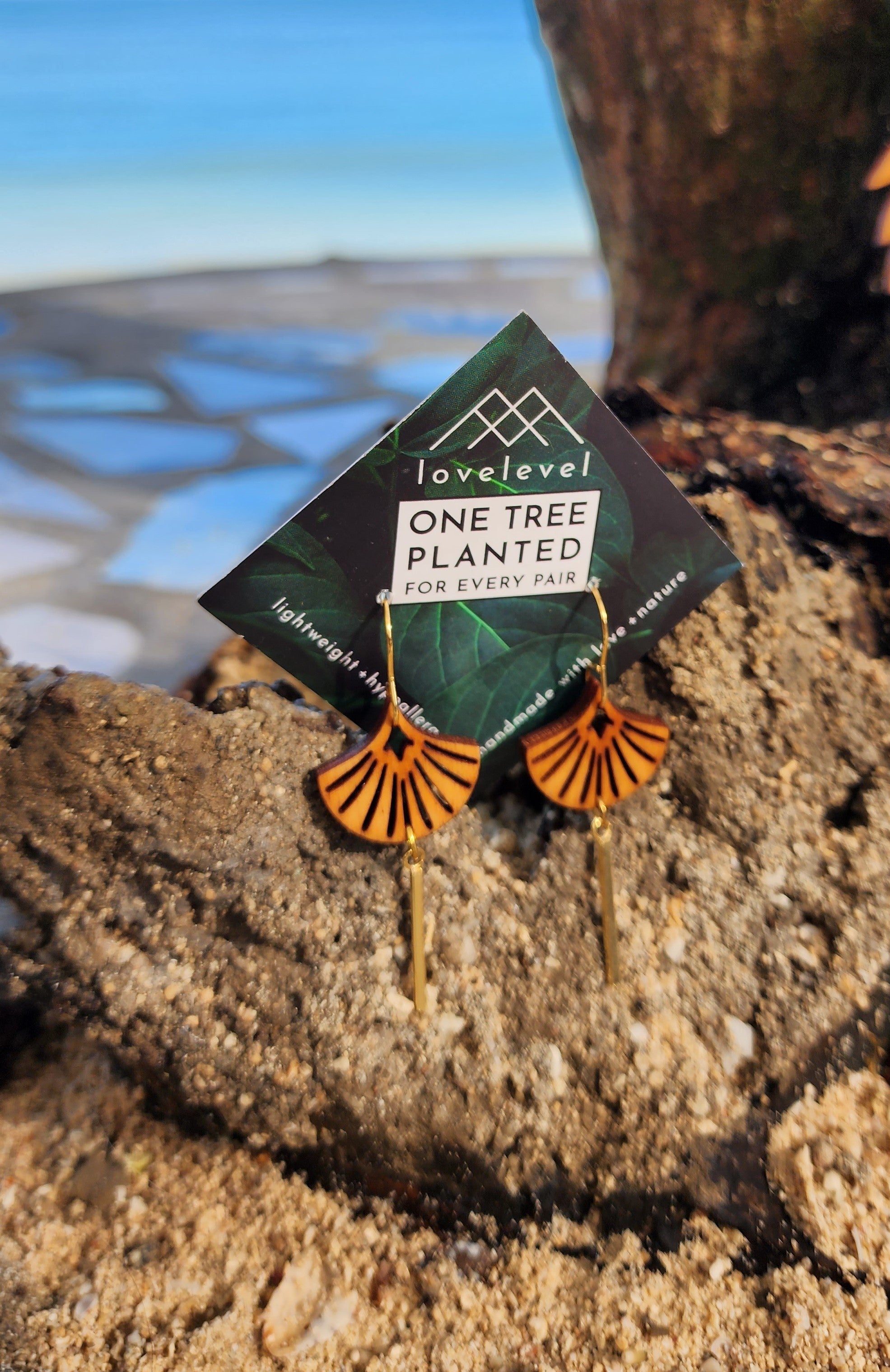 Wooden art deco shell earrings with a gold bar hanging down from the shell on a card with "lovelevel" branding on a rock.