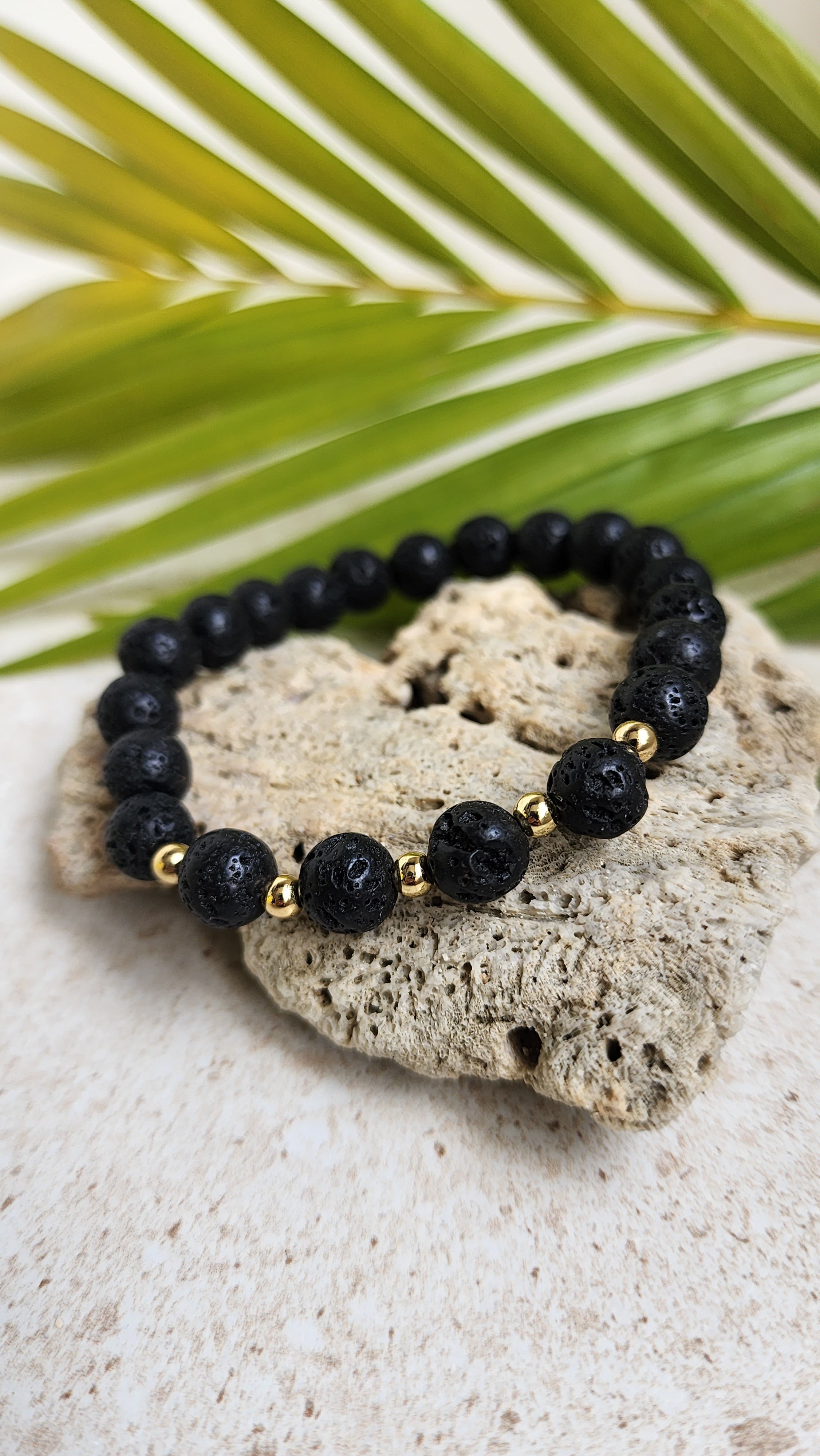 Lava stone bracelet resting along a heart shaped stone with a palm leaf in the background.
