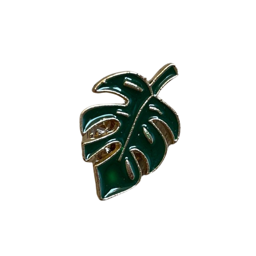 A green and gold Monstera enamel pin with a detailed leaf design.