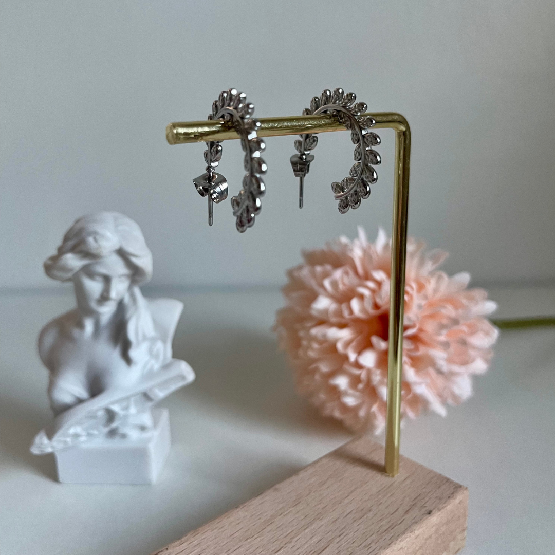 Silver hoop earrings draped over a gold bar with a statue and pink flower in the background.