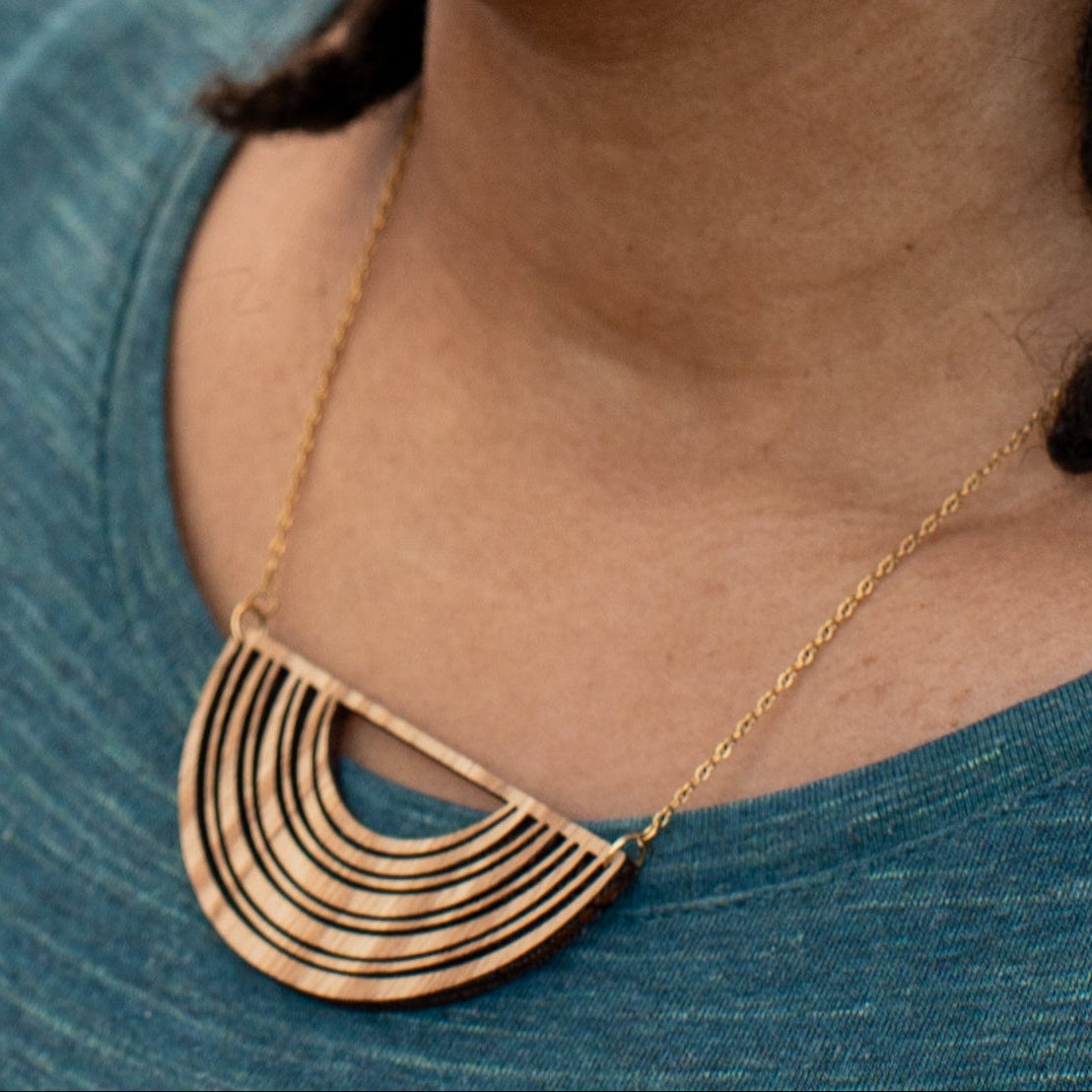 Close up of a wooden necklace with a geographic design worn by person in blue crew neck.
