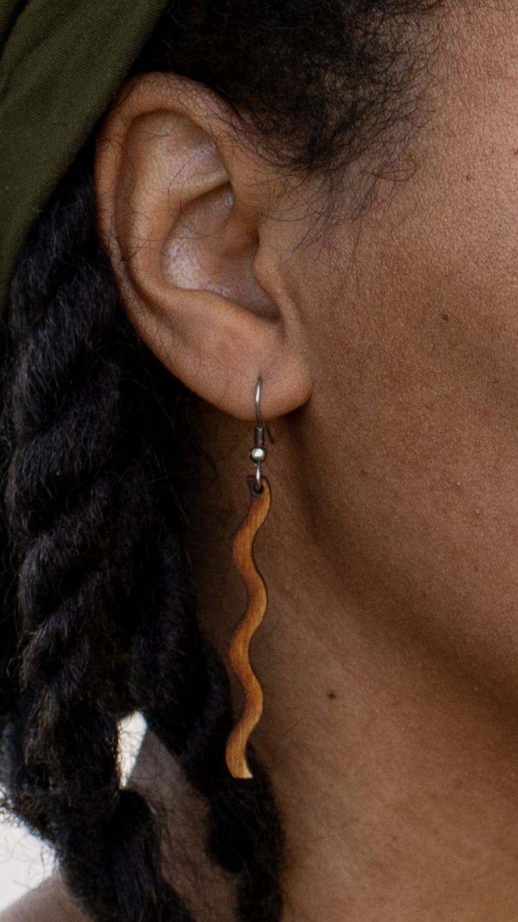 Close up of an ear with a wooden dangle earring and braided hair.