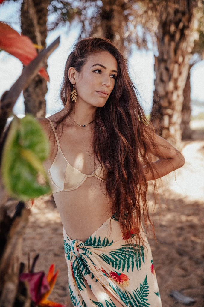 Woman in a tropical dress standing outdoors with trees and sunlight.
