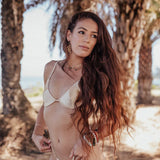 Woman in a white bikini standing among palm trees