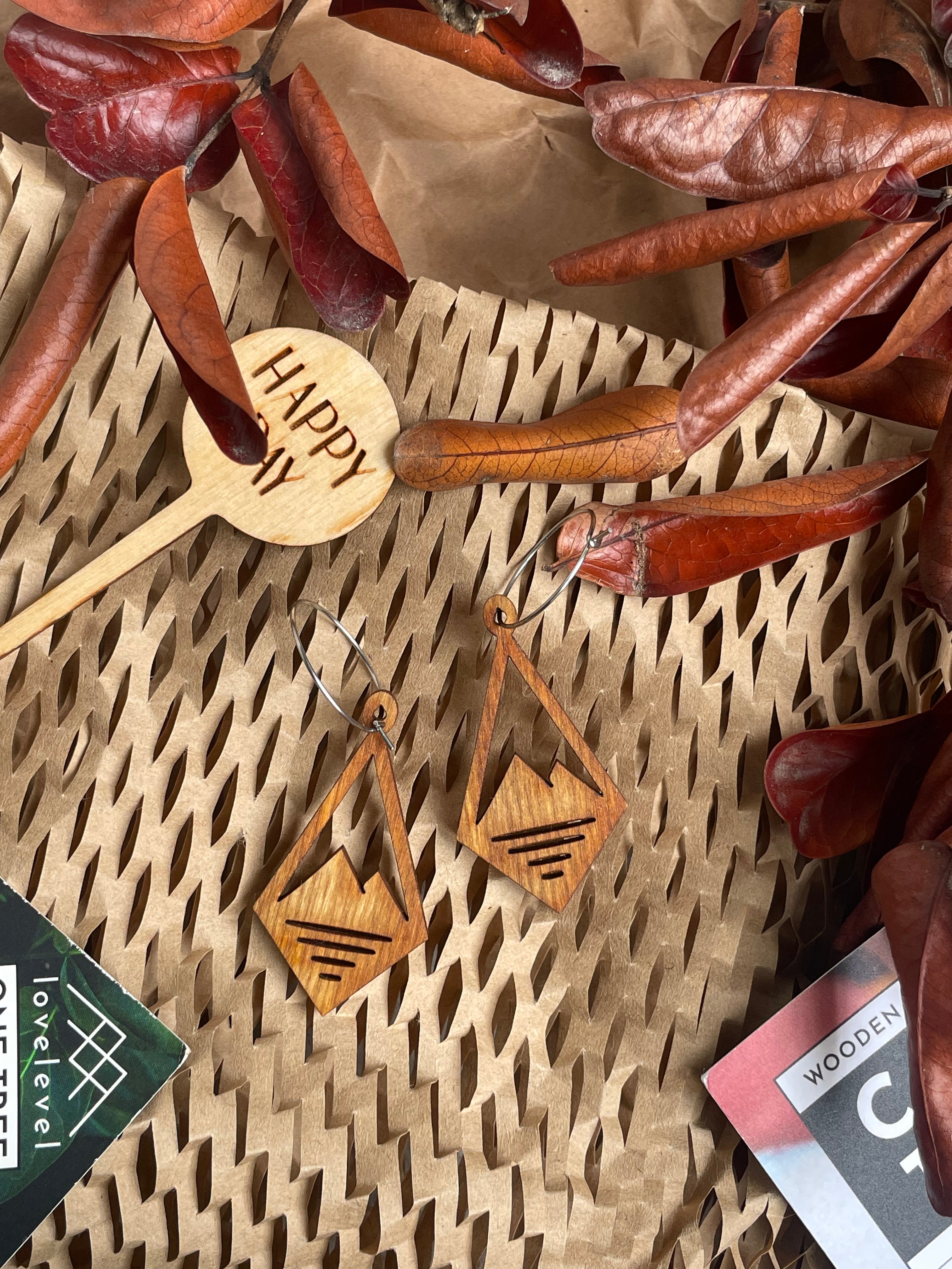 Wooden dangle earrings with mountain peak design and three slits cut out at the base of the mountain, against a natural background.