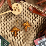 Wooden mushroom dangle earrings against a natural background with dried leaves.