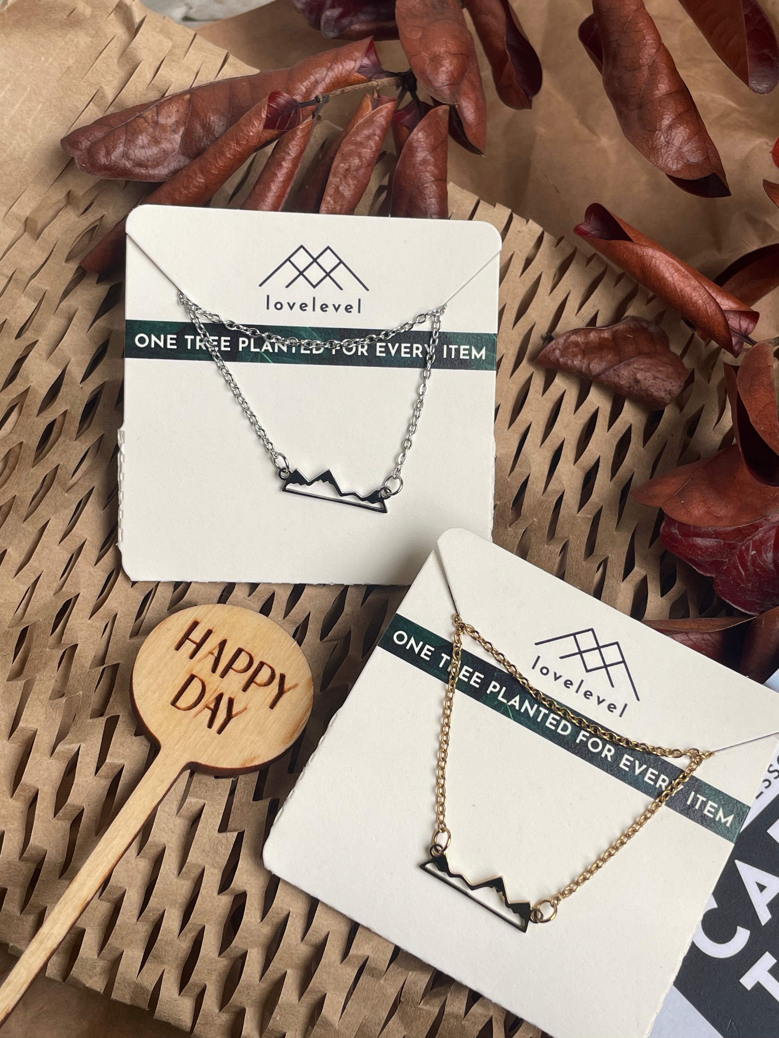 Mountain peak necklaces on cards with 'lovelevel' branding against a natural background.