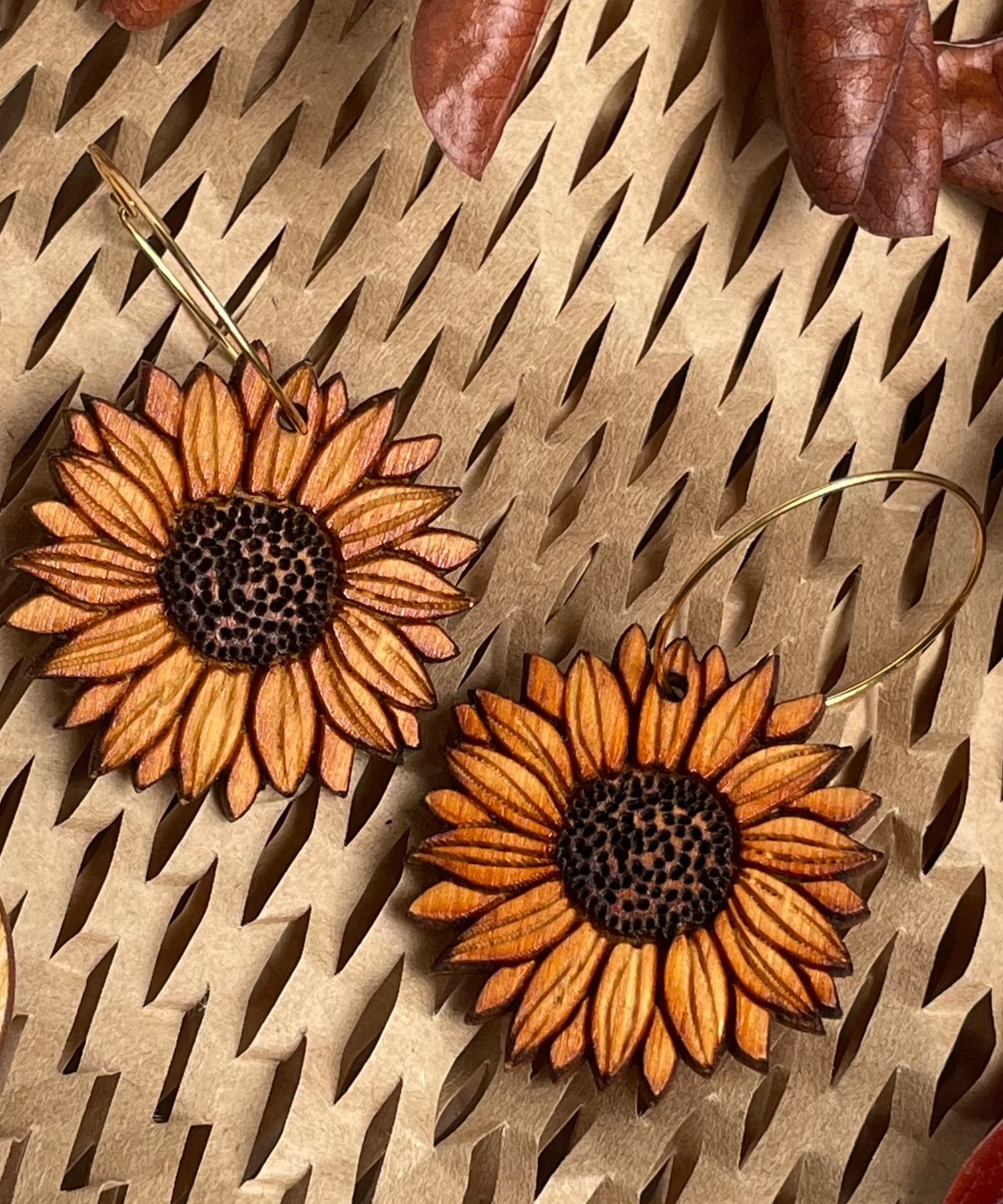 Wooden sunflower earrings on a textured surface with dried leaves.