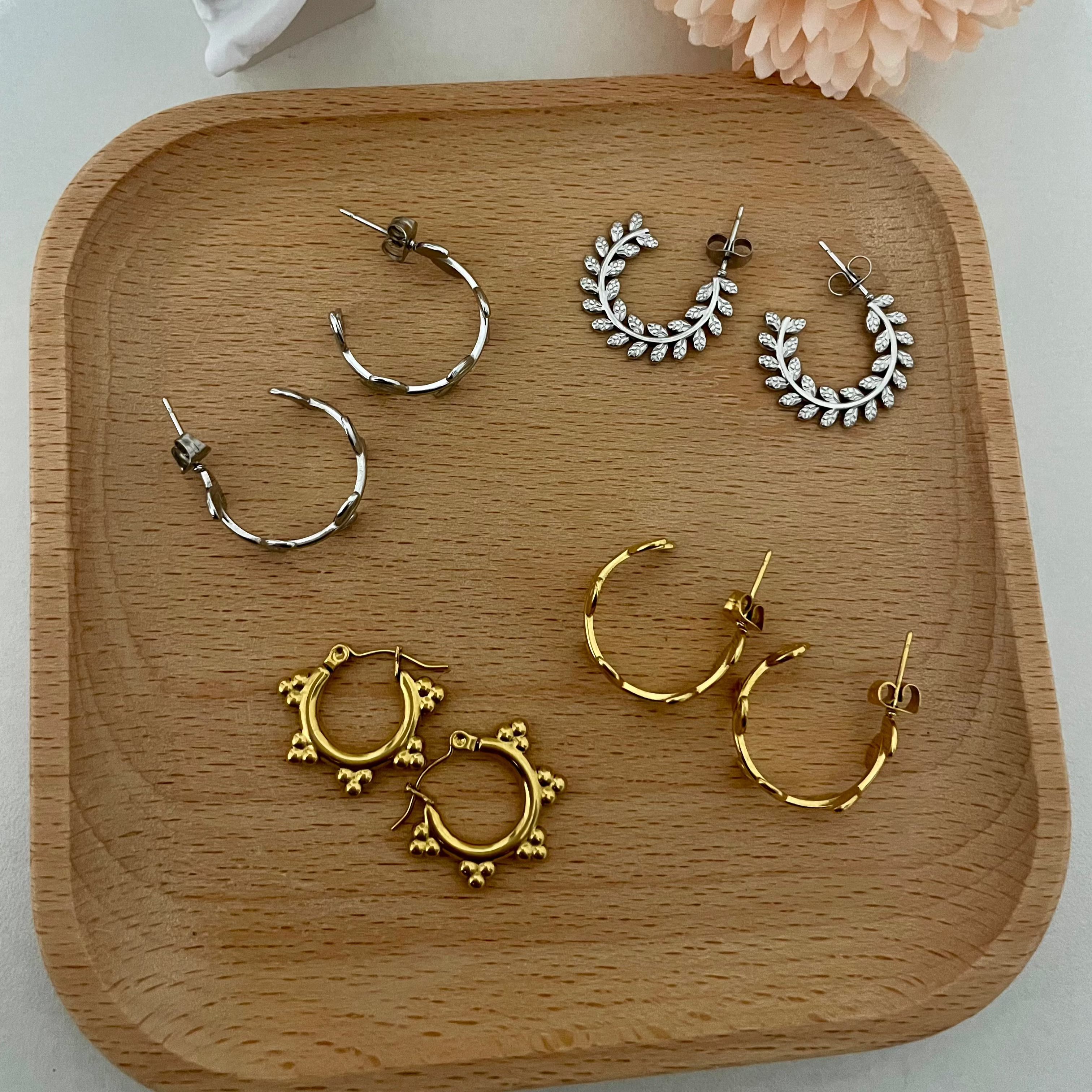 Set of hoop earrings on a wooden tray with a flower and statue in the background