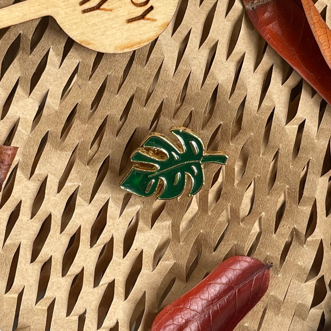 Gold and green enamel Monstera pin on a natural background.
