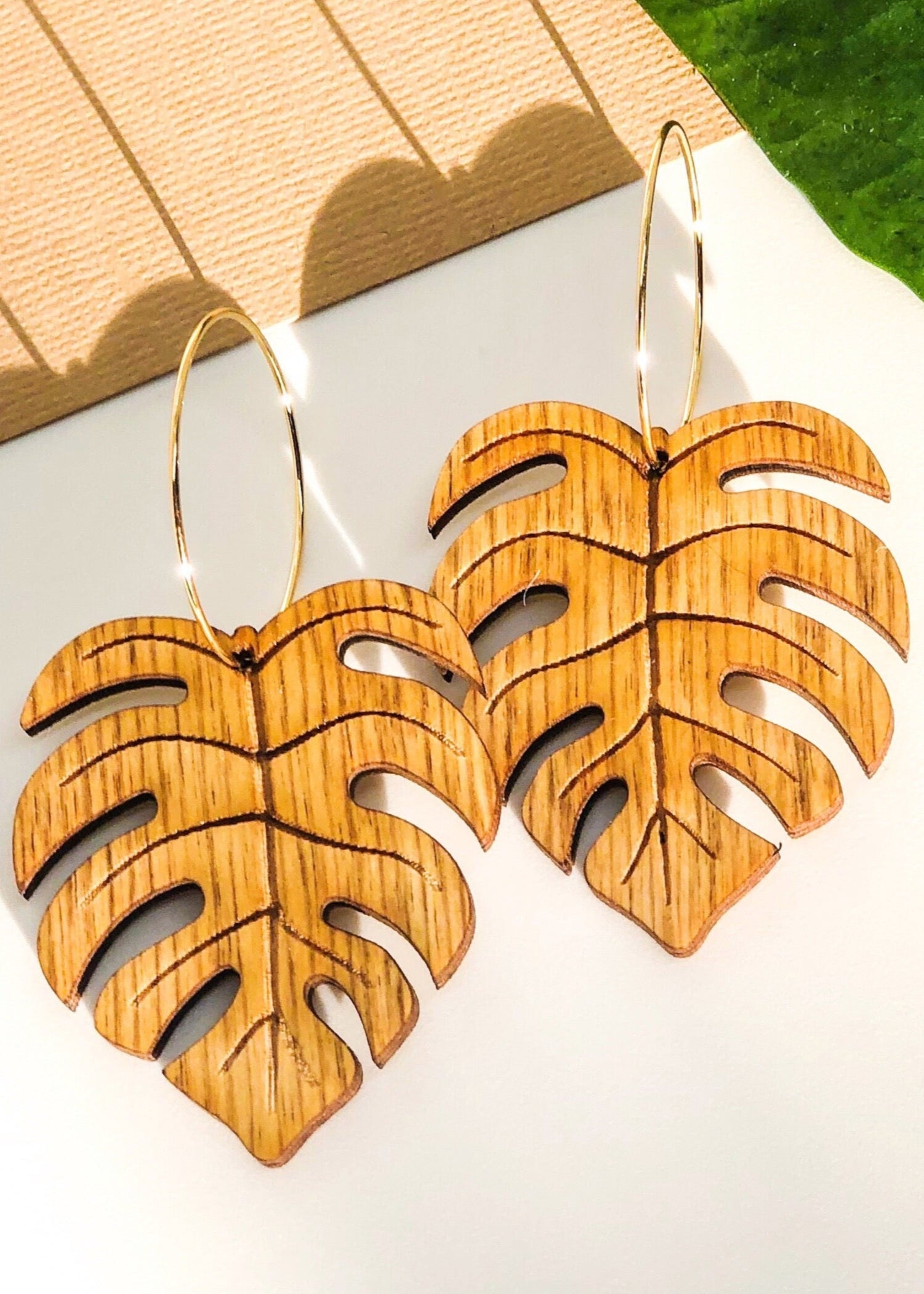 Wooden leaf-shaped earrings on a white surface with a green leaf background