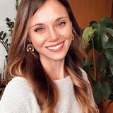 Smiling women in knitted sweater wearing arch earrings against office background.