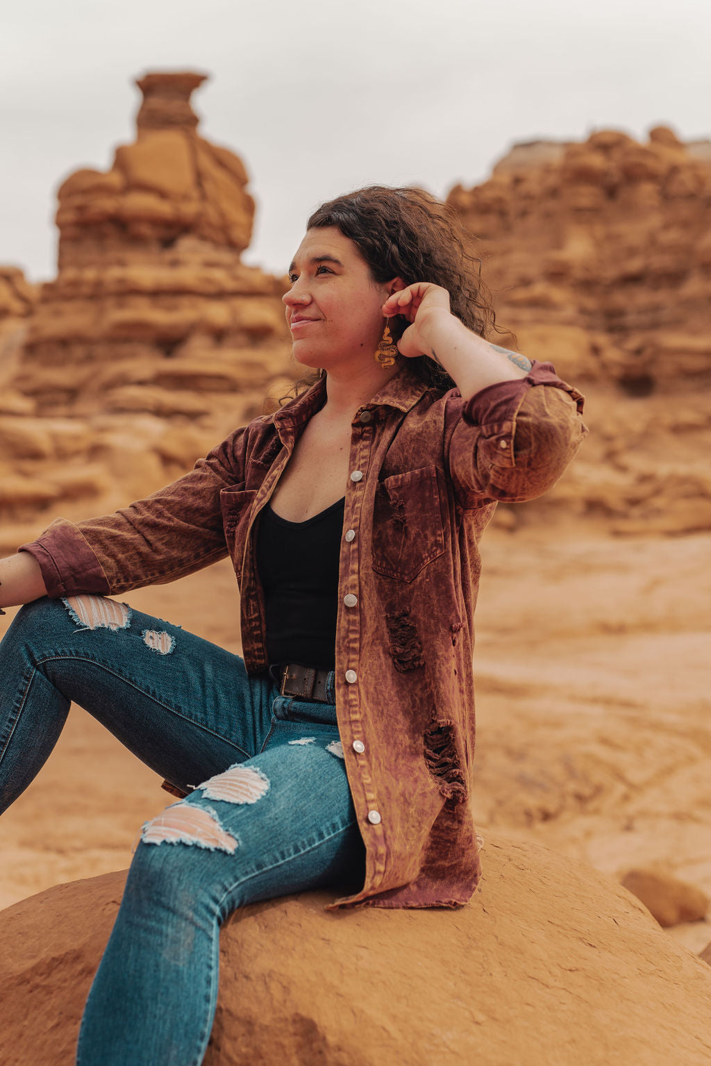 Woman sitting on a rock in a desert landscape with red rock formations.