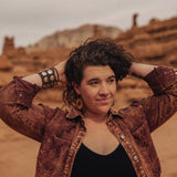 Person with curly hair and sunflower earrings standing in a desert landscape with rock formations.