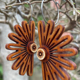 Wooden burst-shaped earrings hanging on a branch with a natural background