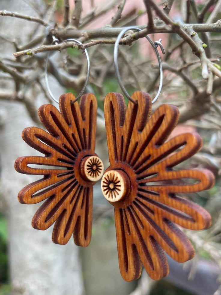 Wooden burst-shaped earrings hanging on a branch with a natural background