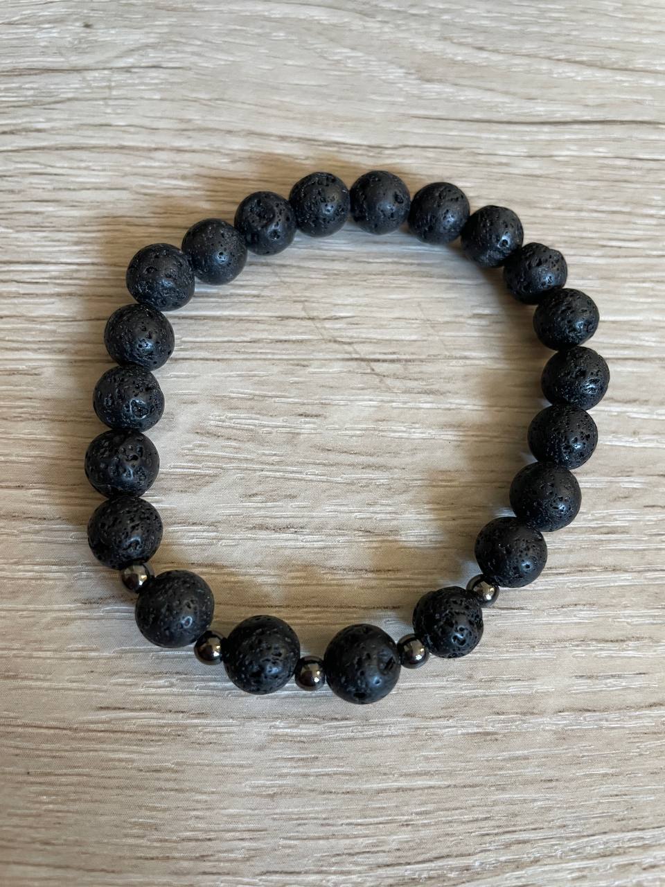Lava stone bracelet with 5 black metal beads against a wooden background.