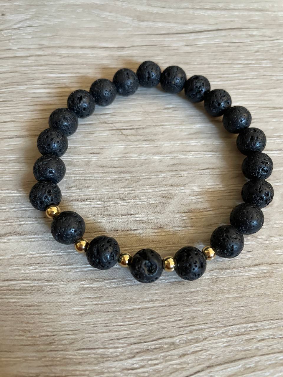 Lava stone bracelet with 5 gold beads against a wooden background.