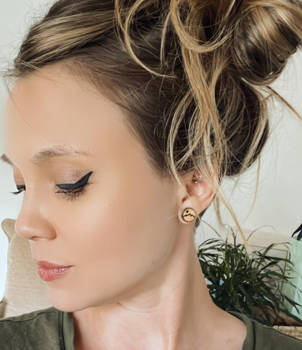 Woman with messy bun wearing wooden stud earring with a mountain peak etched into it.