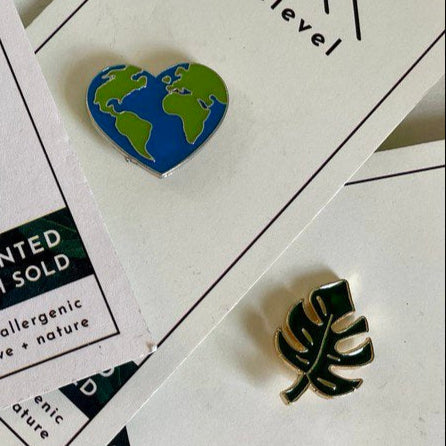 Heart-shaped Earth pin and leaf-shaped pin on a white surface with text.