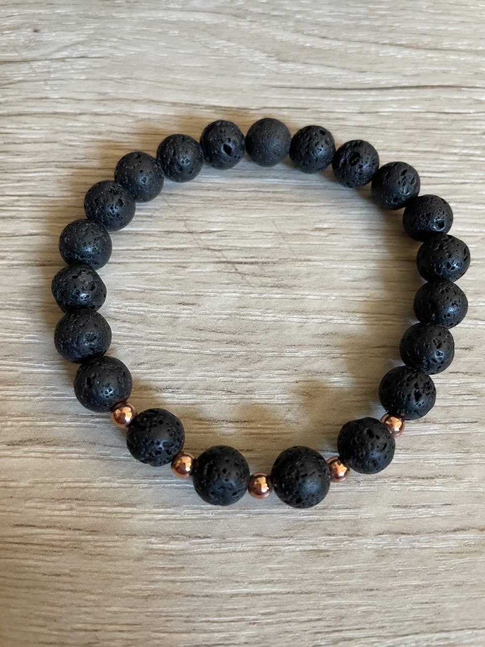 Lava stone bracelet with 5 rose gold beads against a wooden background.