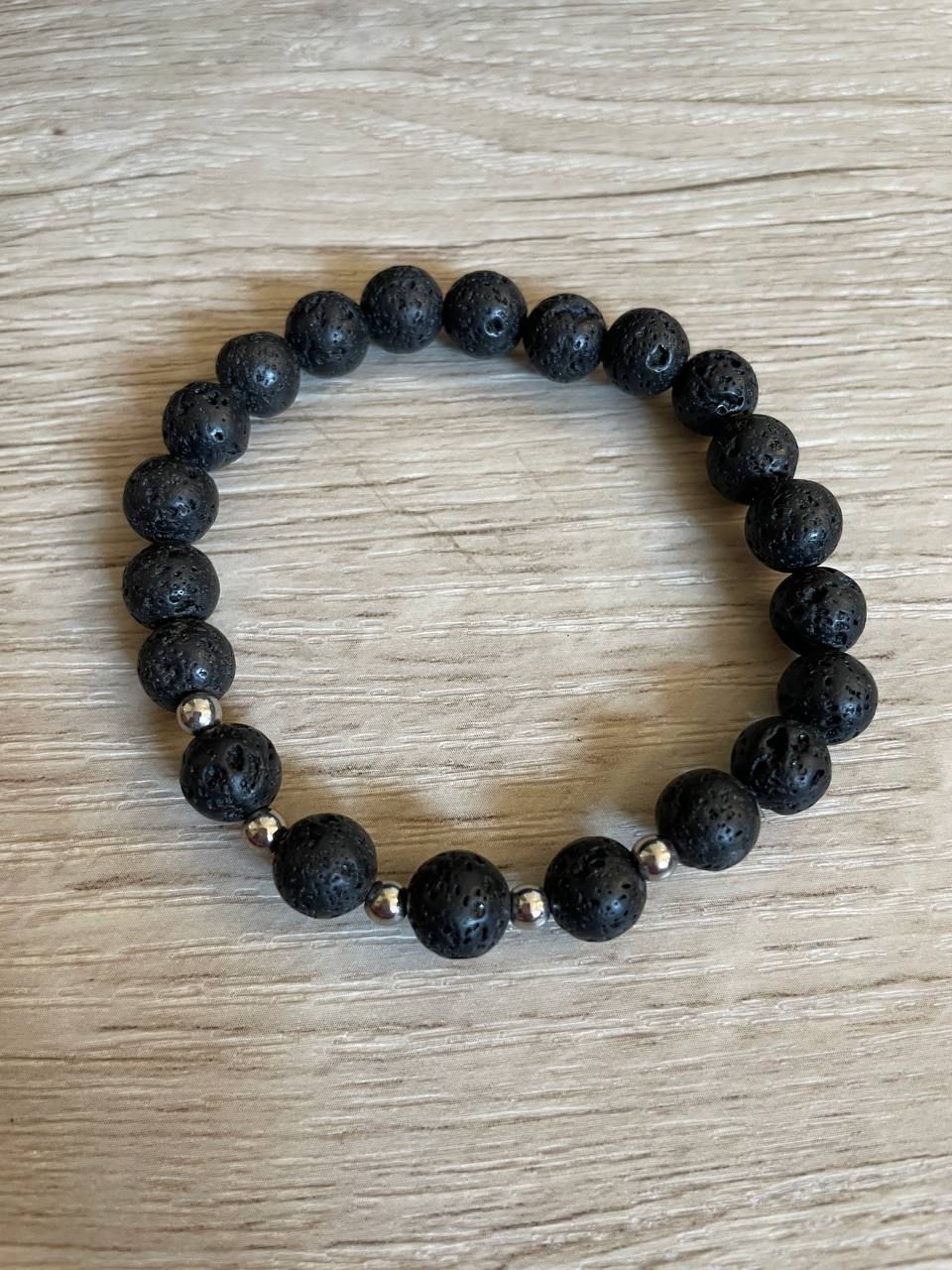 Lava stone bracelet with 5 silver beads against a wooden background.