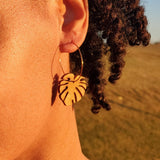 Woman wearing wooden leaf-shaped earrings in a field at sunset