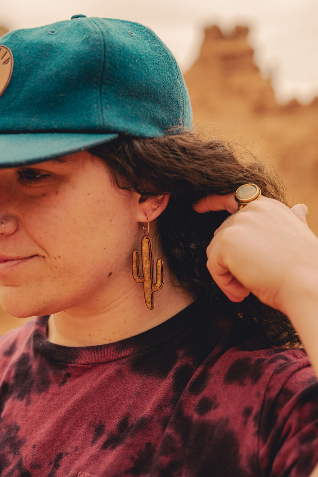 Woman in the desert wearing a blue cap and large wooden cactus earrings.