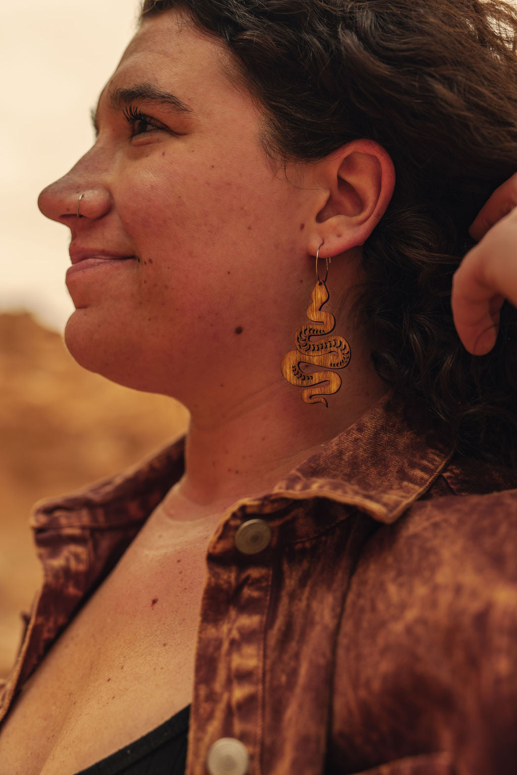 A woman in the desert wearing large wooden snake earrings.