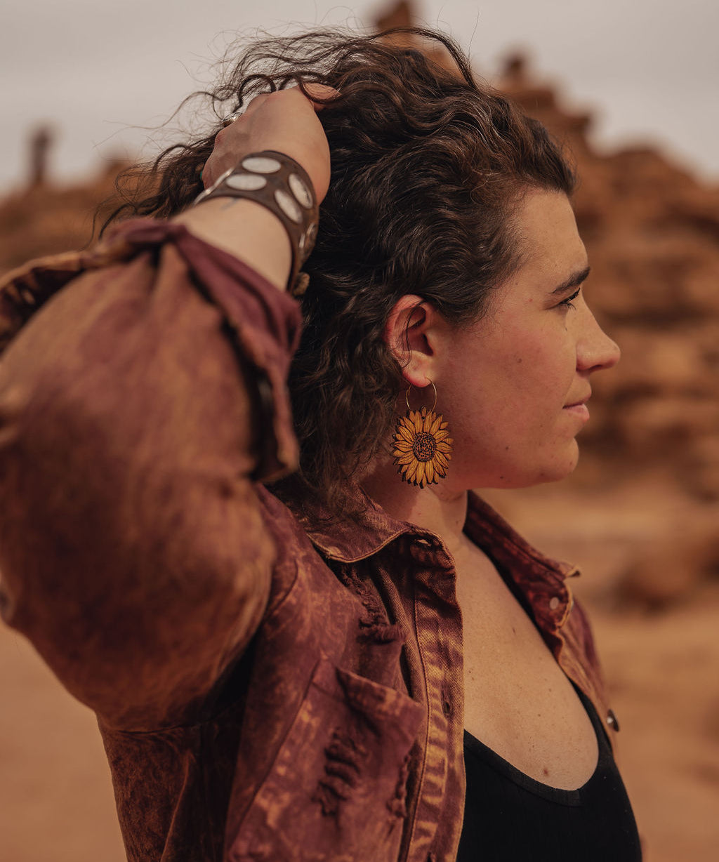 Woman standing out in the desert wearing large wooden sunflower earrings.