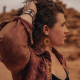 Woman standing out in the desert wearing large wooden sunflower earrings.