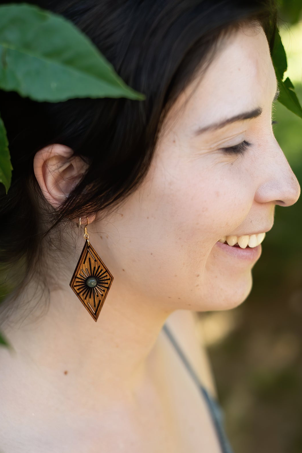 Woman wearing a decorative wooden earring with leaves in the background