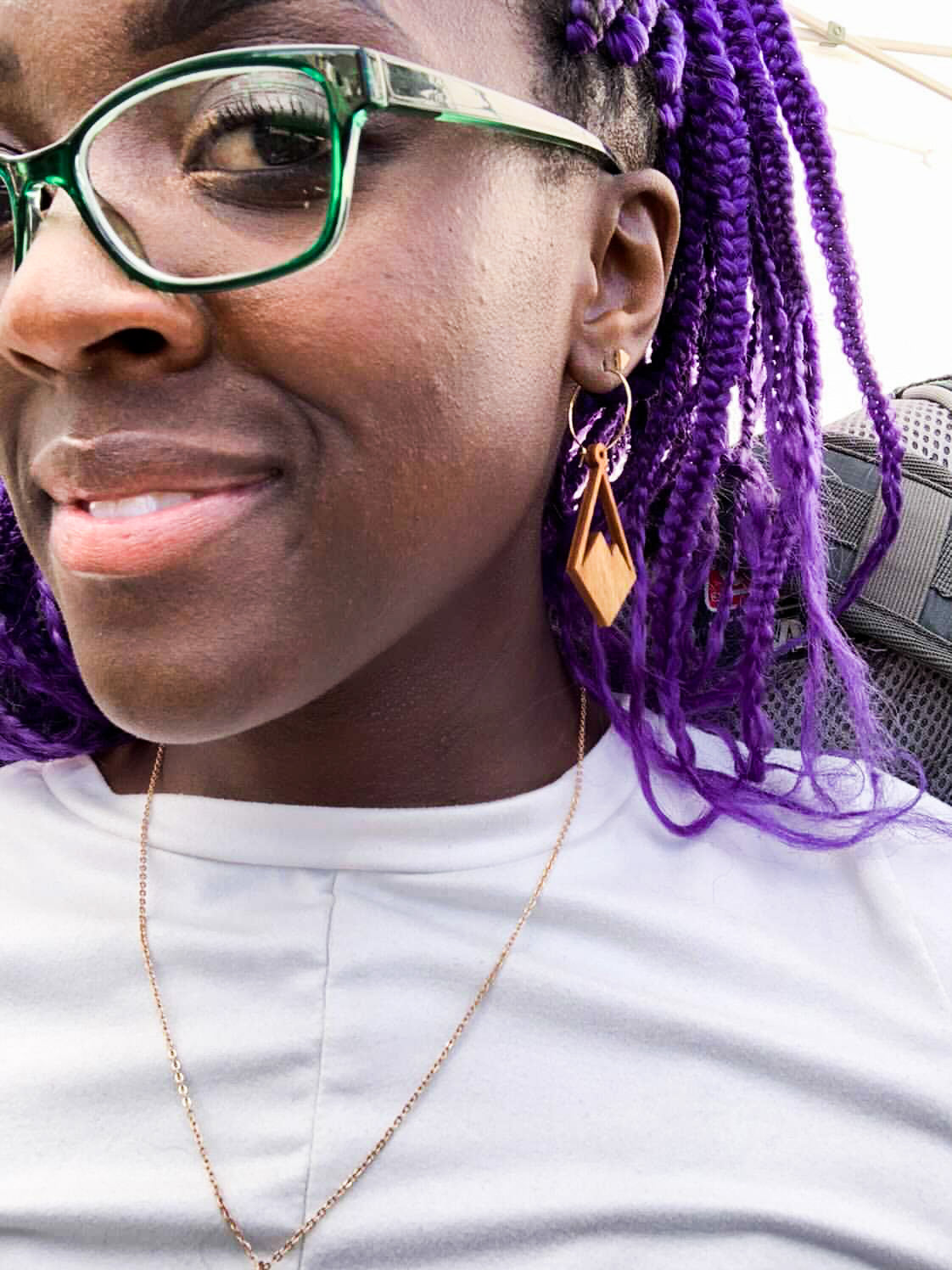 Woman with purple hair wearing diamond shaped wooden earrings with mountain peaks carved in the center.