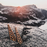 Pair of geometric wooden earrings resting in the crack of a beach rock.