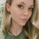 Light haired woman smiling wearing a wooden stud earring with a blue stone in the center.