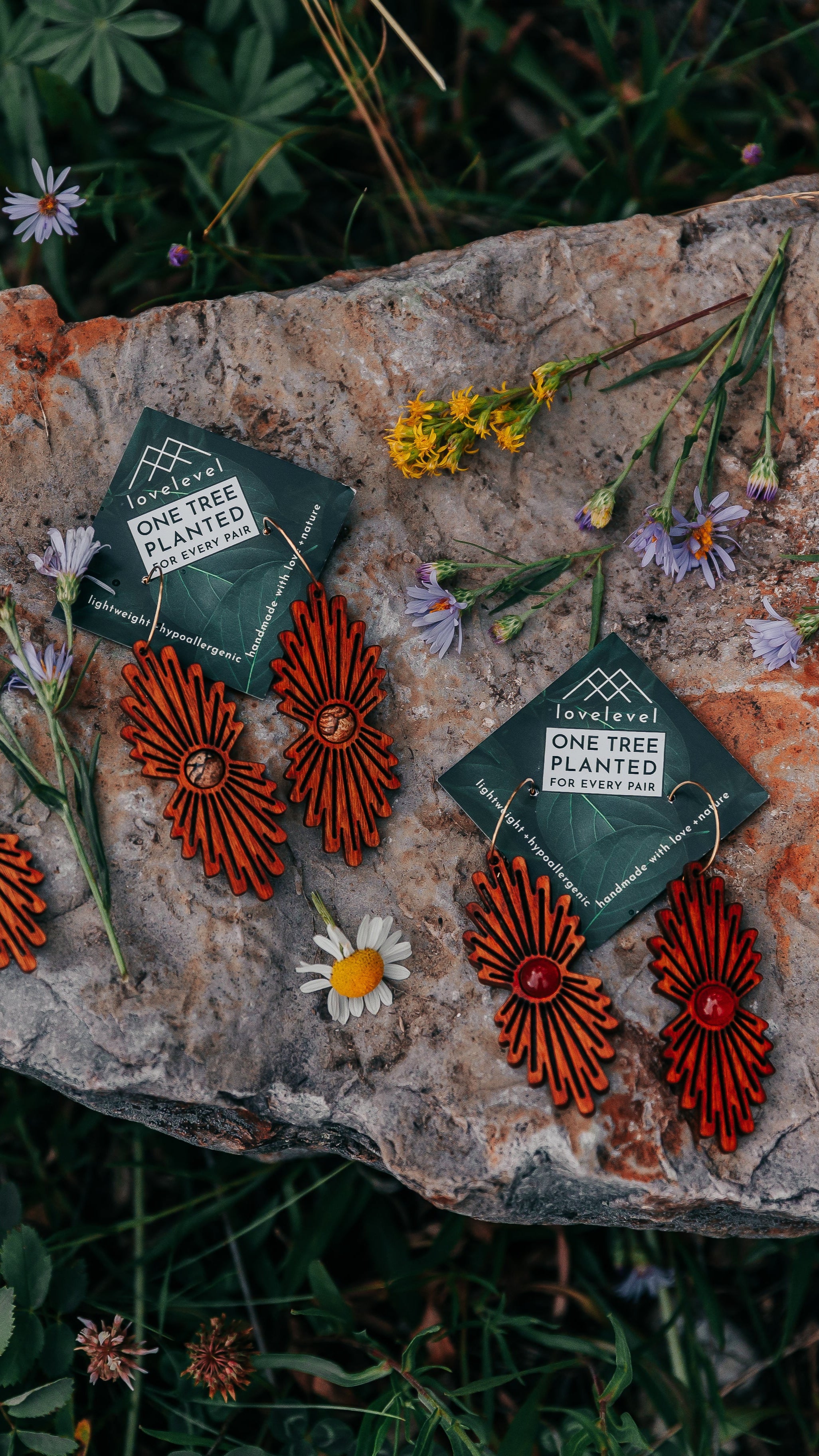 Wooden earrings with a stone center and carved ray bursts on a stone with wildflowers in the background