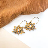Wooden lotus flower earrings on a white background in front of brown fabric.