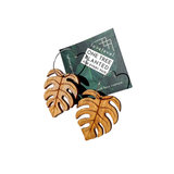 A pair of large wooden earrings carved in the shape of a Monstera leaf on a card with 'lovelevel' branding.