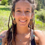Smiling woman in dreads wearing wooden leaf-shaped earrings and a black tank top.