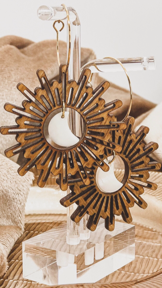 Wooden earrings with sunburst design and moon charm in the center on a beige fabric background