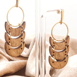 Gold hoop earrings with wooden crescent ornaments on a clear stand with beige fabric in the background