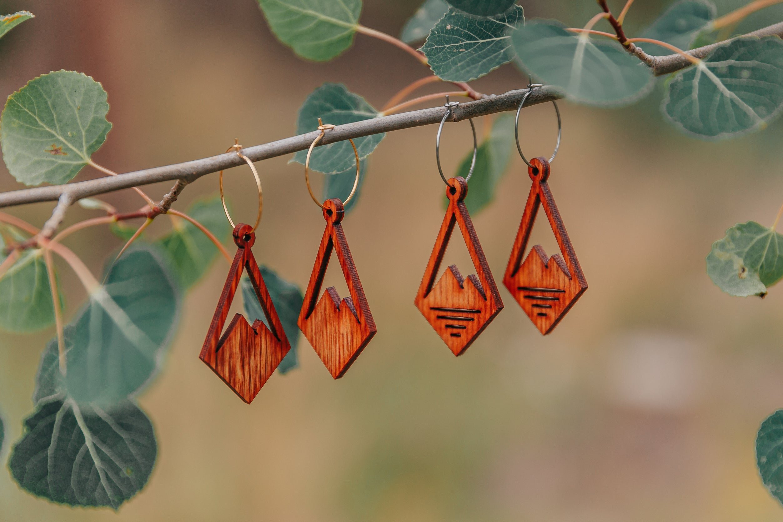 Two pairs of wooden diamond earrings with a mountain peak carved into the center, one with three slits cut out in the base of the mountain.