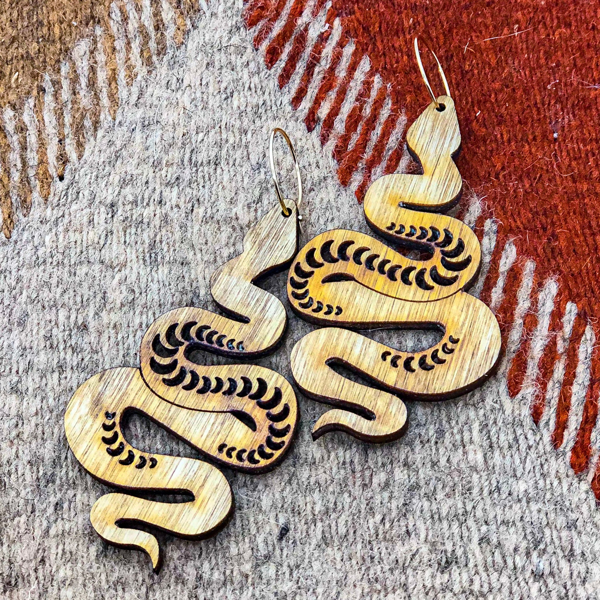 A pair of wooden snake earrings on top of a geometric carpet.