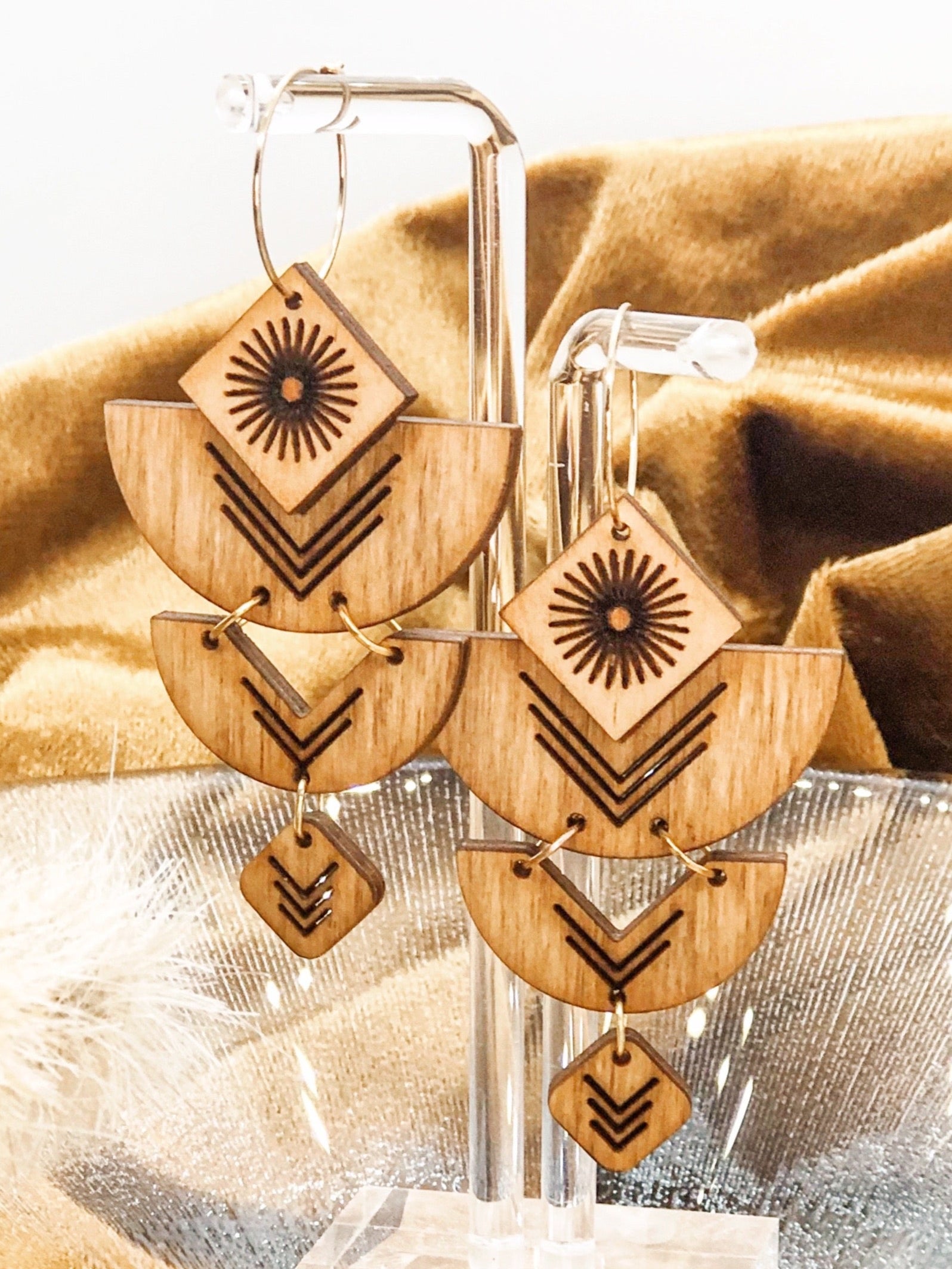 Wooden earrings with geometric designs on a stand in front of golden fabric.