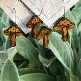 Two pairs of wooden mushroom shaped earrings on cards with 'lovelevel' branding in front of a natural background.