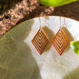 Pair of wooden geometric diamond earrings on a stone plate.