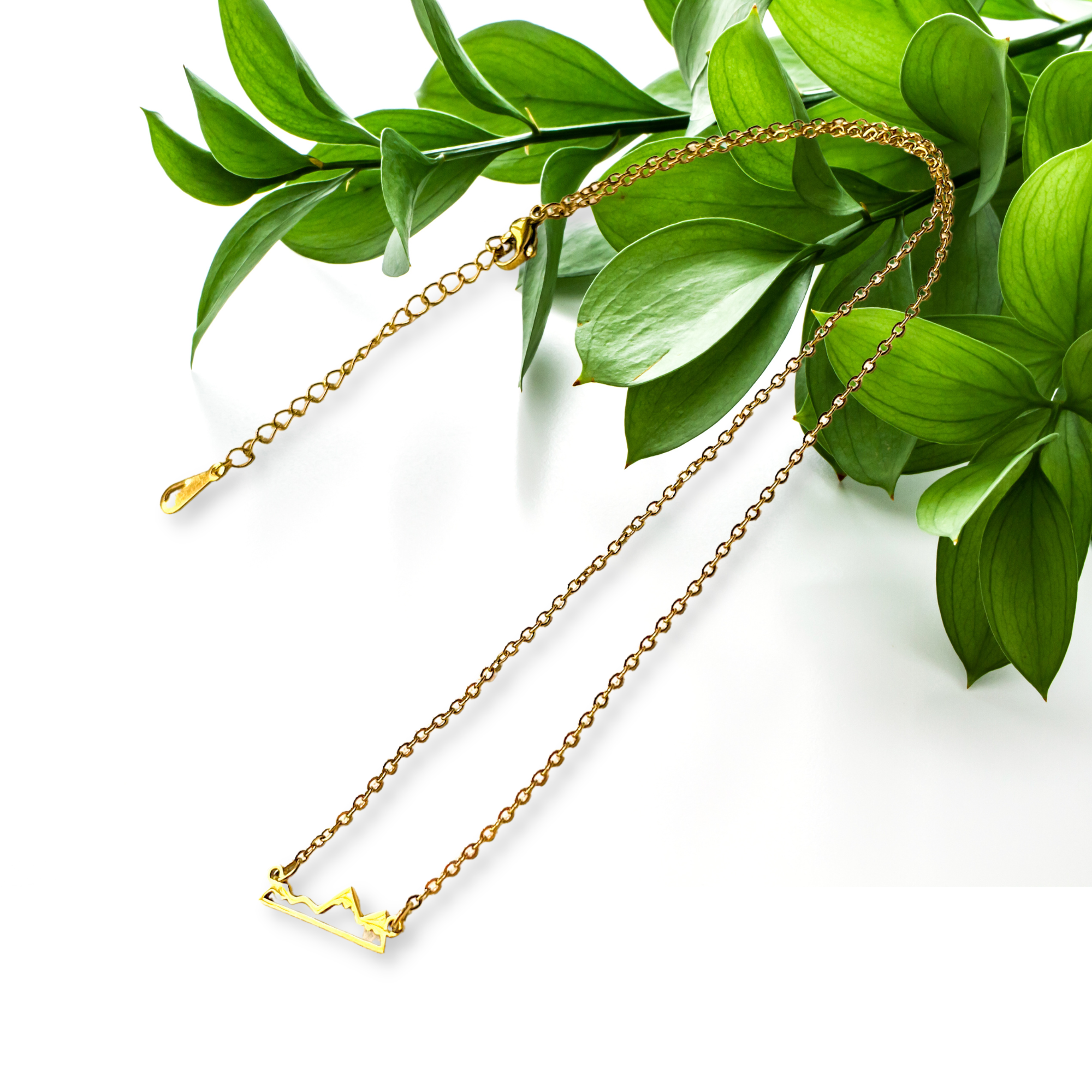 Necklace with a golden mountain silhouette charm draped from green leaves.