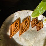 Two pairs of wooden geometric diamond earrings sitting on a stone plate.