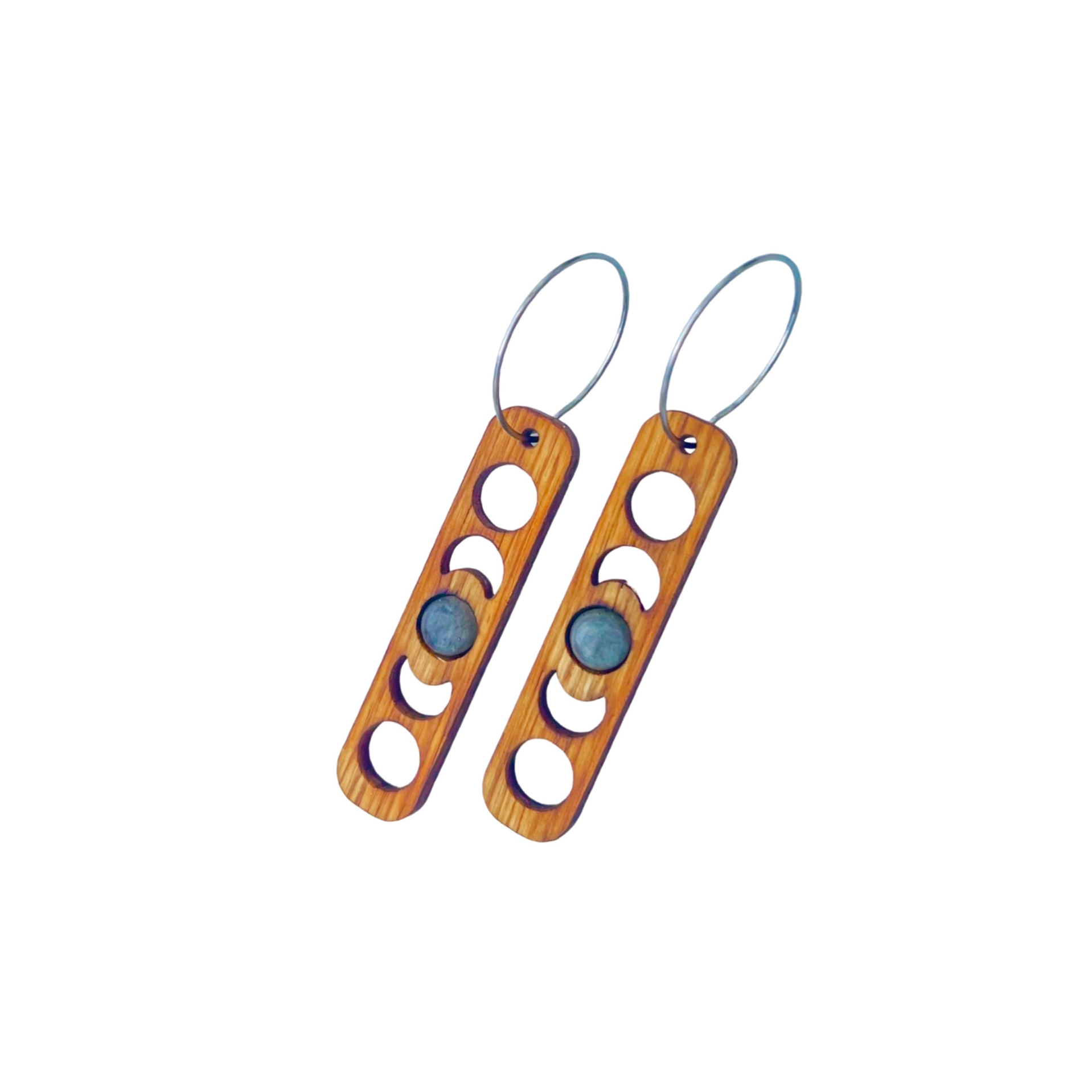 Wooden earrings with moon patterns cut out surrounding a moonstone gem.