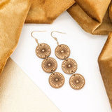 Wooden circular earrings on a white surface surrounded by bronze cloth.